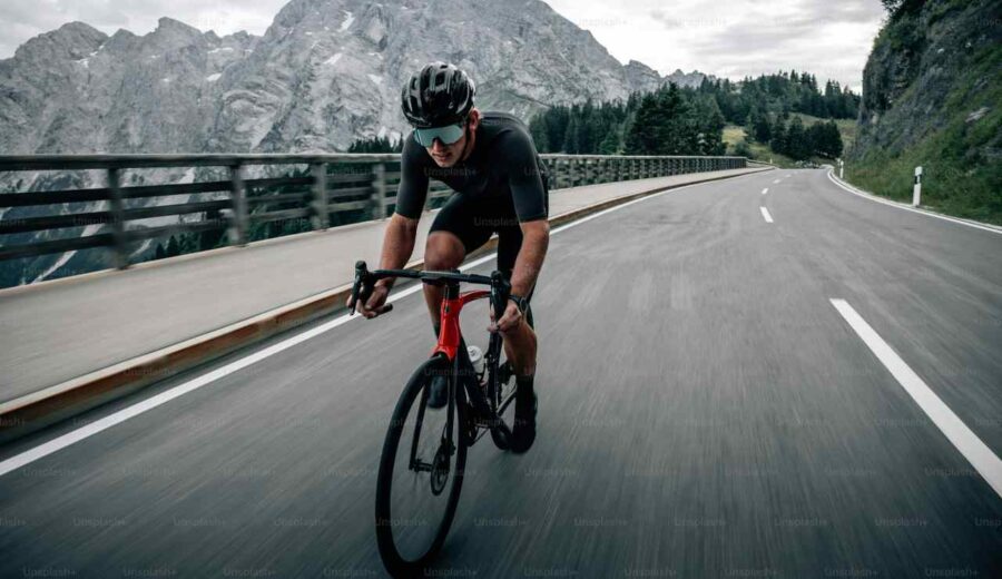 Ciclista percorre una strada (Unsplash)