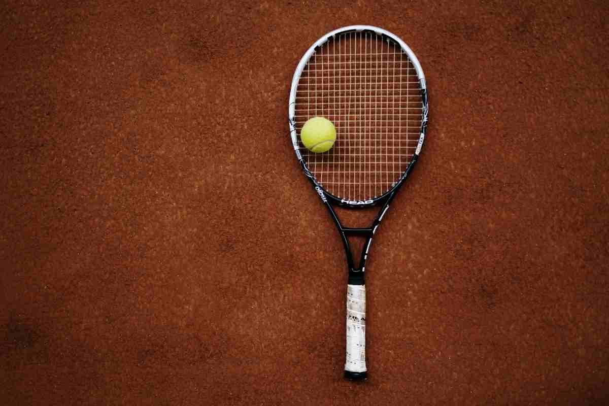 Una racchetta da tennis e una pallina sul campo in terra rossa